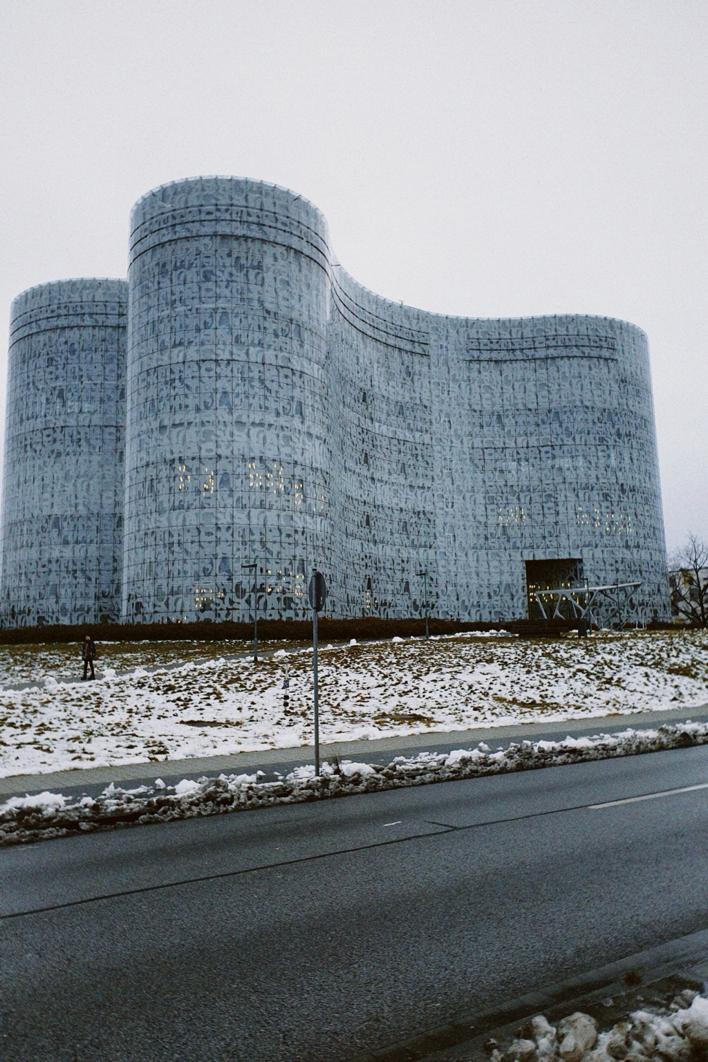 The curved glass facade of the IKMZ University Library in Cottbus above a snow-covered landscape.