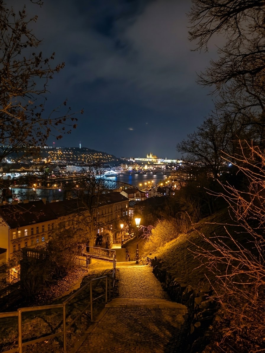 Night view over Prague with illuminated historic buildings, the Vltava River and Charles Bridge.